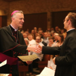 bishop joseph williams shakes the hand of a seminarian