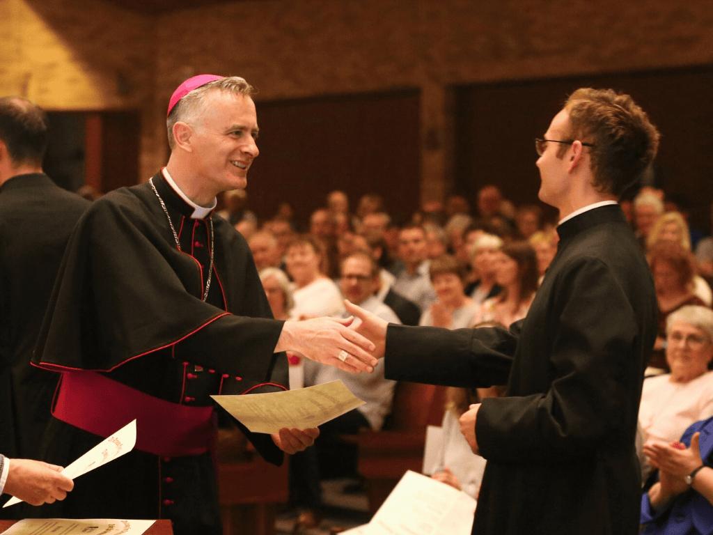 bishop joseph williams shakes the hand of a seminarian