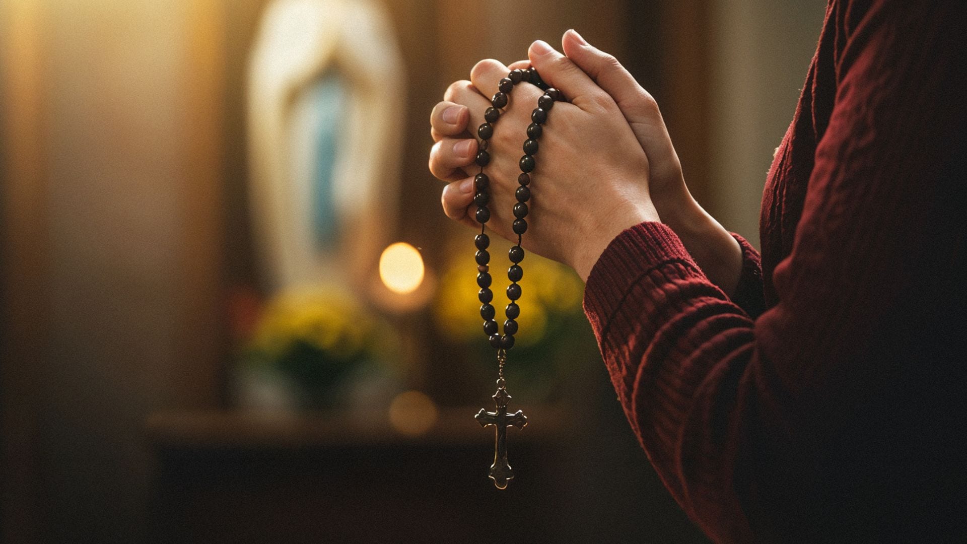 folded hands with rosary in front of mary statue during lent