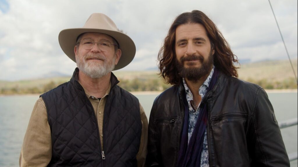 jeff cavins and jonathan roumie smile next the sea of galilee in the holy land