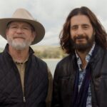 jeff cavins and jonathan roumie smile next the sea of galilee in the holy land